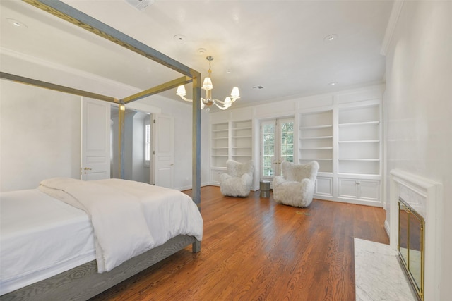 bedroom featuring hardwood / wood-style flooring, ornamental molding, a high end fireplace, and an inviting chandelier