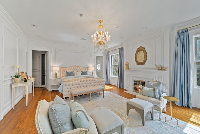 bedroom featuring a decorative wall, crown molding, a fireplace with flush hearth, light wood-style flooring, and a notable chandelier