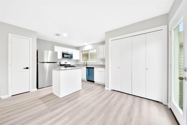 kitchen featuring white cabinetry, a center island, stainless steel appliances, light stone countertops, and light wood-type flooring