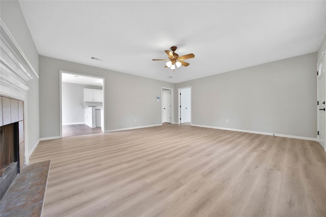 unfurnished living room with a tiled fireplace, ceiling fan, and light wood-type flooring