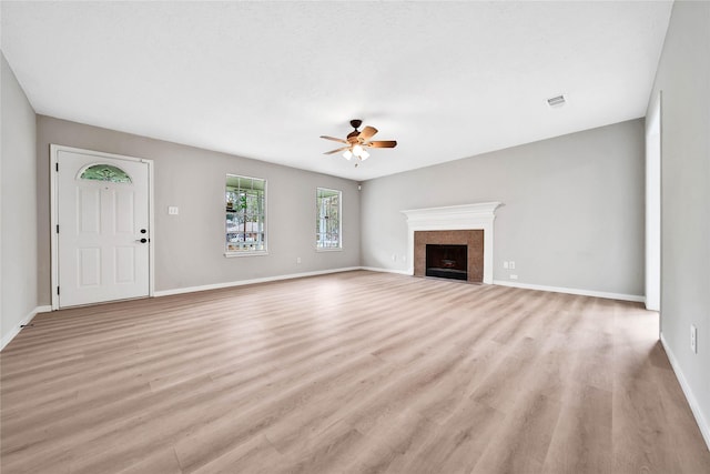 unfurnished living room with a tile fireplace, ceiling fan, and light wood-type flooring