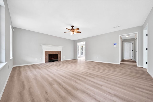 unfurnished living room with ceiling fan, a tiled fireplace, and light wood-type flooring