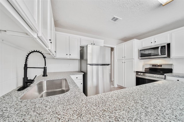 kitchen featuring stainless steel appliances, white cabinetry, sink, and light stone counters