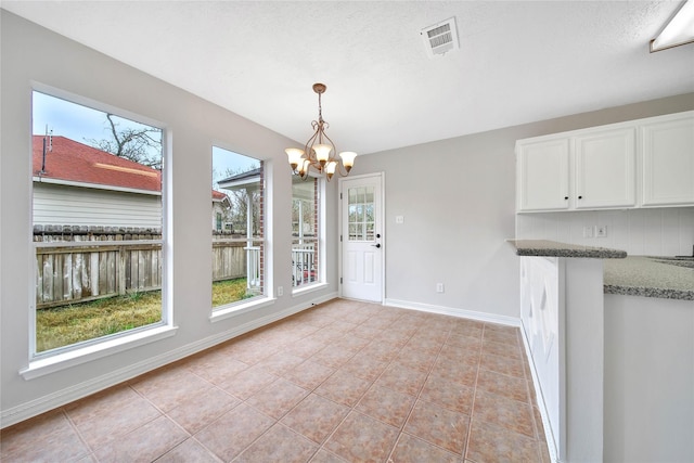 unfurnished dining area featuring an inviting chandelier, light tile patterned floors, and a textured ceiling