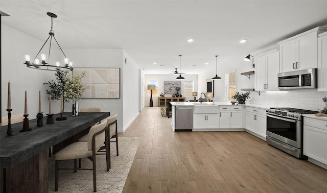 kitchen featuring pendant lighting, stainless steel appliances, light hardwood / wood-style floors, and white cabinets