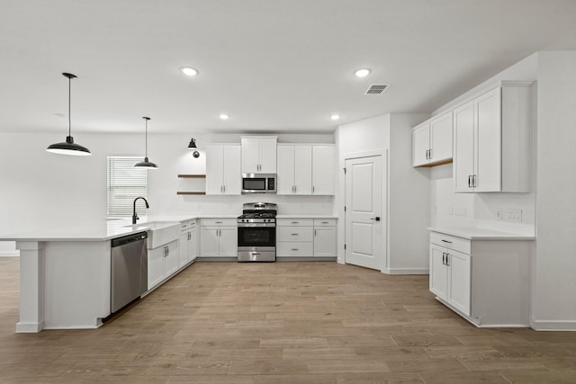 kitchen featuring sink, light hardwood / wood-style flooring, hanging light fixtures, stainless steel appliances, and white cabinets