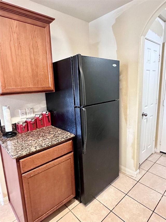 kitchen featuring light tile patterned floors, dark stone counters, and black fridge