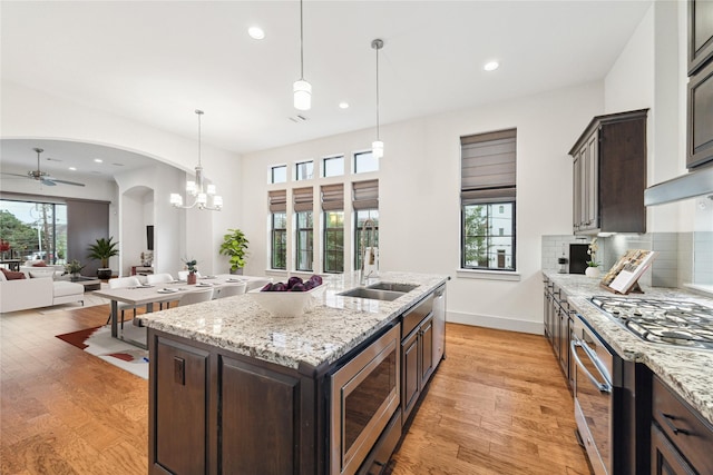 kitchen with sink, dark brown cabinets, light wood-type flooring, appliances with stainless steel finishes, and an island with sink