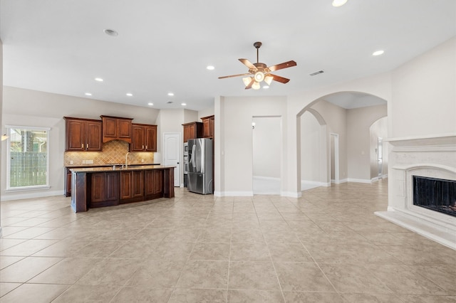 kitchen featuring sink, stainless steel fridge with ice dispenser, an island with sink, ceiling fan, and decorative backsplash