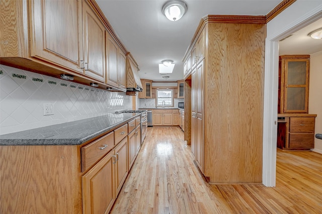 kitchen featuring sink, decorative backsplash, light hardwood / wood-style floors, and dark stone counters