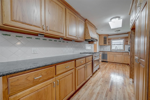 kitchen with sink, light hardwood / wood-style flooring, stainless steel appliances, tasteful backsplash, and dark stone counters