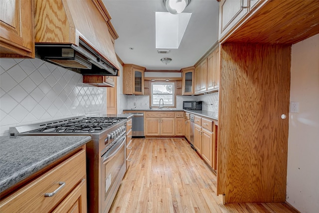 kitchen featuring sink, decorative backsplash, stainless steel appliances, custom range hood, and light wood-type flooring