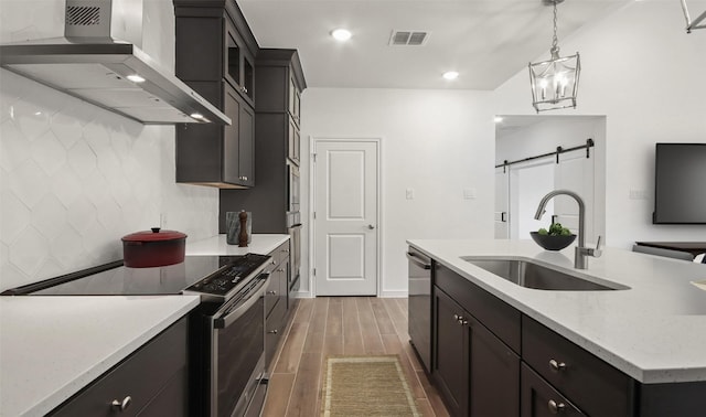 kitchen featuring appliances with stainless steel finishes, sink, hanging light fixtures, a barn door, and wall chimney range hood