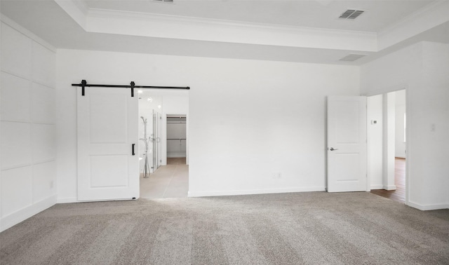 carpeted spare room featuring crown molding, a barn door, and a raised ceiling