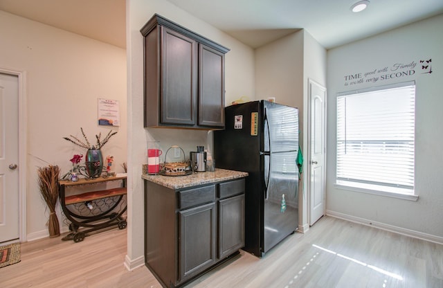 kitchen featuring light stone countertops, black fridge, dark brown cabinets, and light hardwood / wood-style floors