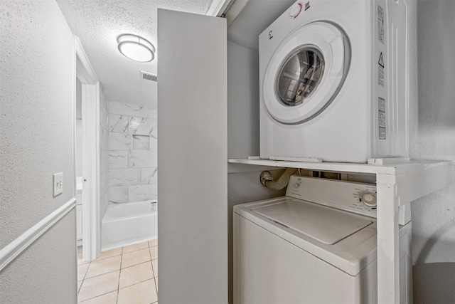 laundry room with light tile patterned flooring, stacked washer / drying machine, and a textured ceiling