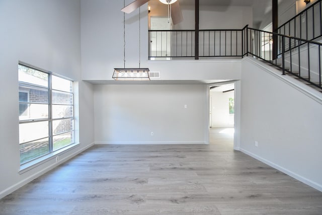 interior space with ceiling fan, a towering ceiling, and light hardwood / wood-style floors