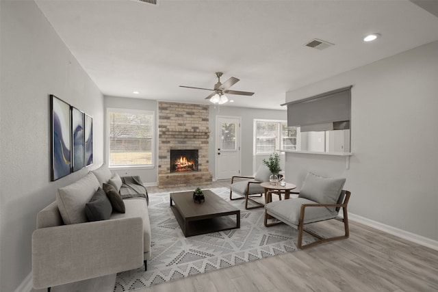 living room with ceiling fan, plenty of natural light, a fireplace, and light wood-type flooring