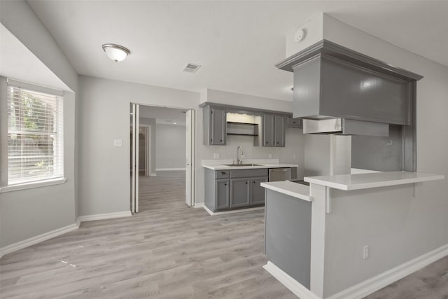 kitchen featuring sink, a breakfast bar area, gray cabinets, kitchen peninsula, and light hardwood / wood-style floors