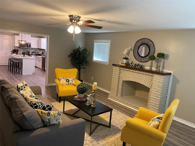 living room with a brick fireplace, hardwood / wood-style flooring, and ceiling fan