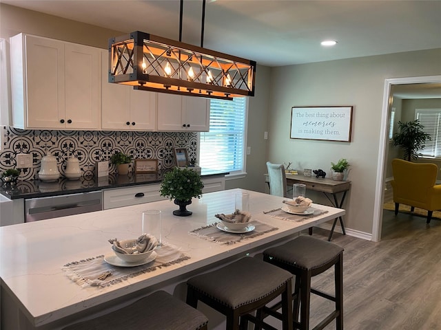 kitchen featuring white cabinetry, wood-type flooring, stainless steel dishwasher, and decorative light fixtures