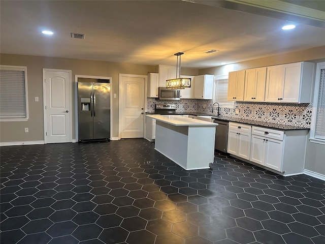 kitchen featuring appliances with stainless steel finishes, pendant lighting, white cabinetry, backsplash, and a center island