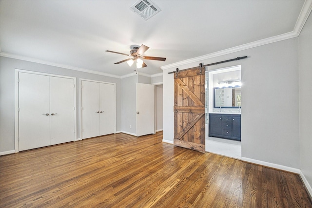 unfurnished bedroom featuring multiple closets, crown molding, a barn door, and dark wood-type flooring