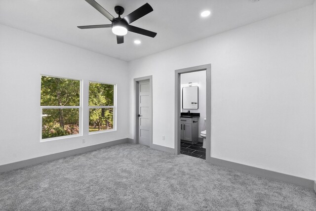 unfurnished bedroom featuring ceiling fan, connected bathroom, and dark carpet