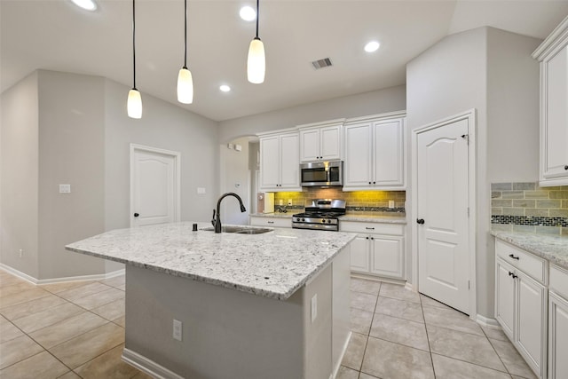 kitchen featuring white cabinetry, sink, stainless steel appliances, light stone countertops, and a center island with sink