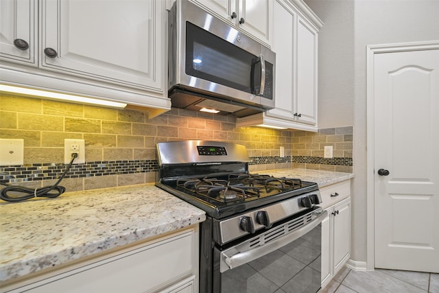 kitchen with light tile patterned flooring, appliances with stainless steel finishes, tasteful backsplash, white cabinets, and light stone countertops