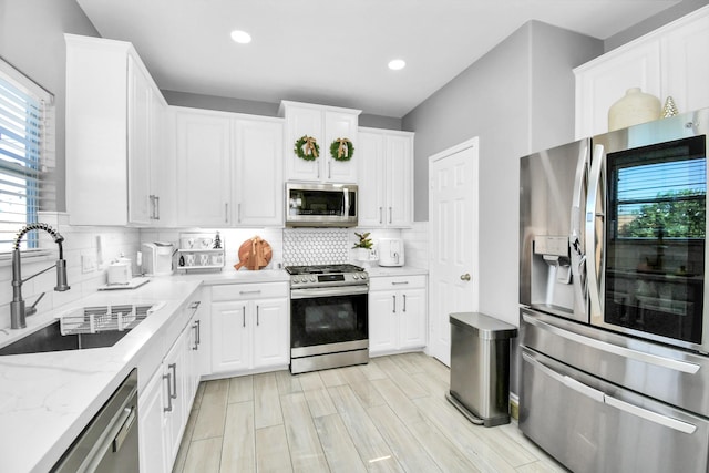 kitchen featuring sink, white cabinetry, tasteful backsplash, stainless steel appliances, and light stone countertops