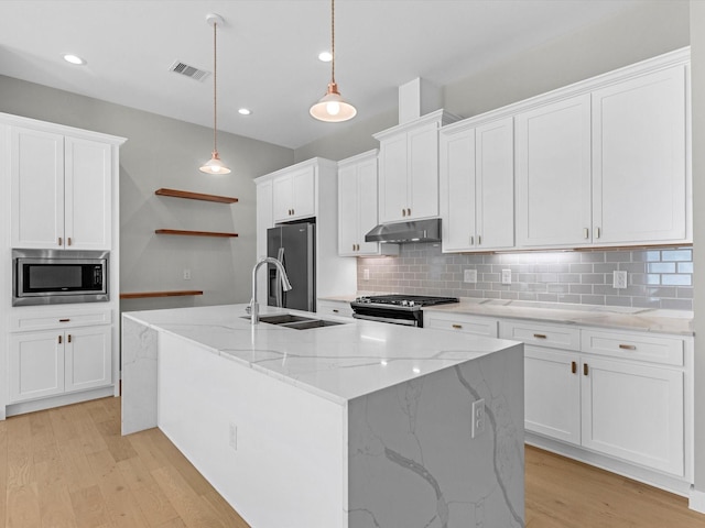 kitchen featuring white cabinetry, light stone counters, hanging light fixtures, stainless steel appliances, and a kitchen island with sink