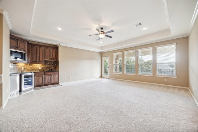 unfurnished living room featuring crown molding, ceiling fan, a tray ceiling, light carpet, and beverage cooler