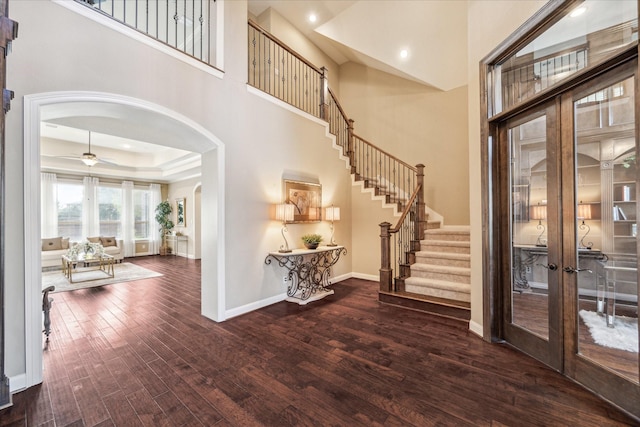 entrance foyer featuring dark wood-type flooring, french doors, ceiling fan, a tray ceiling, and a towering ceiling