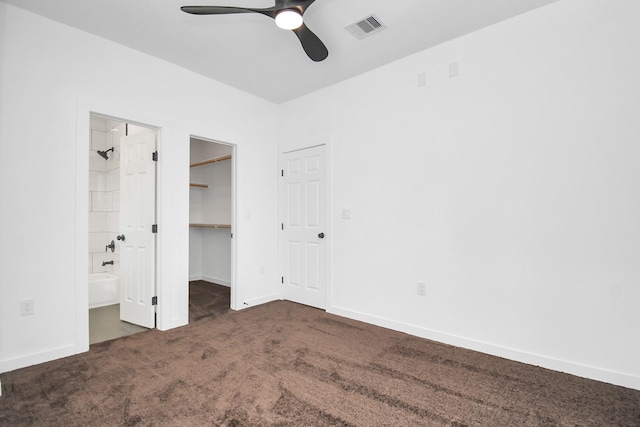 unfurnished bedroom featuring dark colored carpet, ensuite bath, a walk in closet, a closet, and ceiling fan