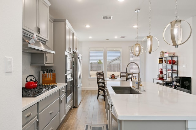 kitchen with stainless steel appliances, sink, an island with sink, and gray cabinetry