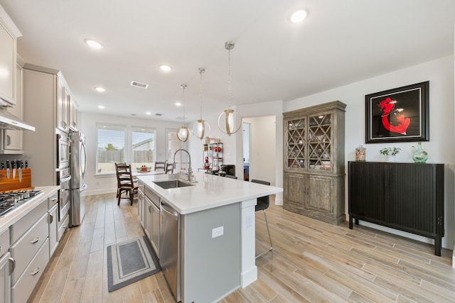 kitchen with a breakfast bar, pendant lighting, an island with sink, sink, and light hardwood / wood-style flooring