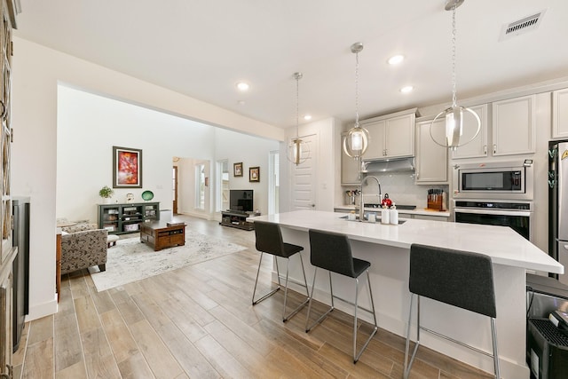 kitchen featuring pendant lighting, a kitchen breakfast bar, stainless steel appliances, light hardwood / wood-style floors, and a center island with sink