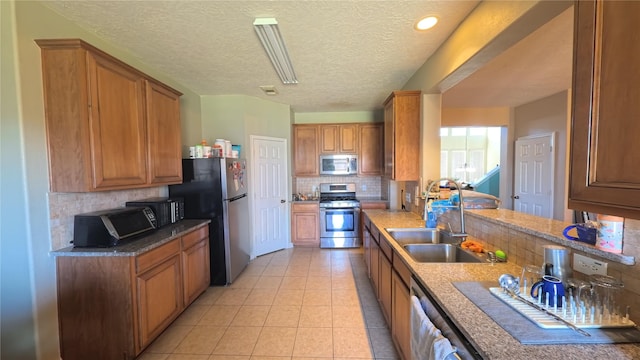 kitchen featuring sink, light tile patterned floors, stainless steel appliances, a textured ceiling, and decorative backsplash