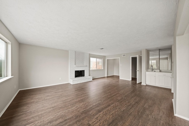 unfurnished living room featuring dark hardwood / wood-style flooring, sink, a brick fireplace, and a textured ceiling