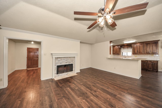 unfurnished living room with dark wood-type flooring, a stone fireplace, sink, ornamental molding, and ceiling fan