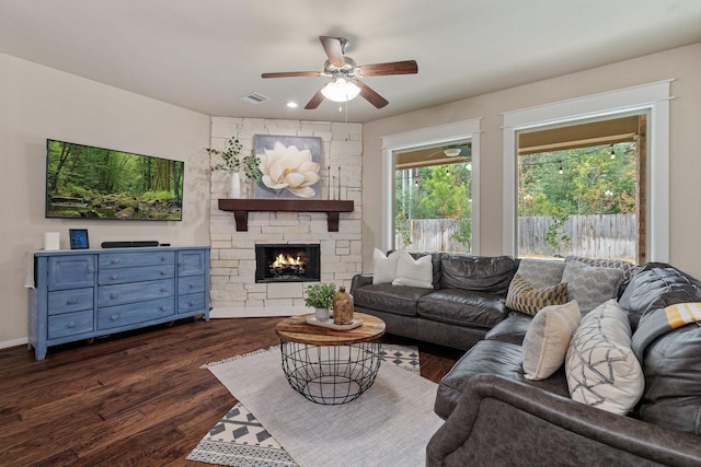 living room with a stone fireplace, dark wood-type flooring, and ceiling fan