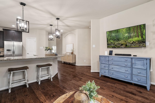 kitchen featuring pendant lighting, stainless steel fridge, a kitchen breakfast bar, light stone counters, and dark hardwood / wood-style flooring