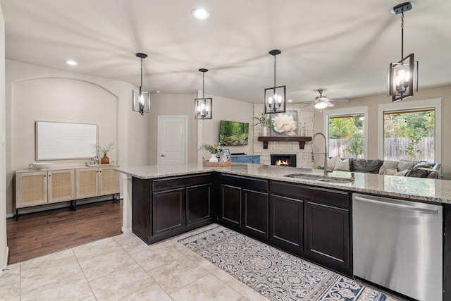 kitchen featuring pendant lighting, sink, dishwasher, light stone counters, and a fireplace