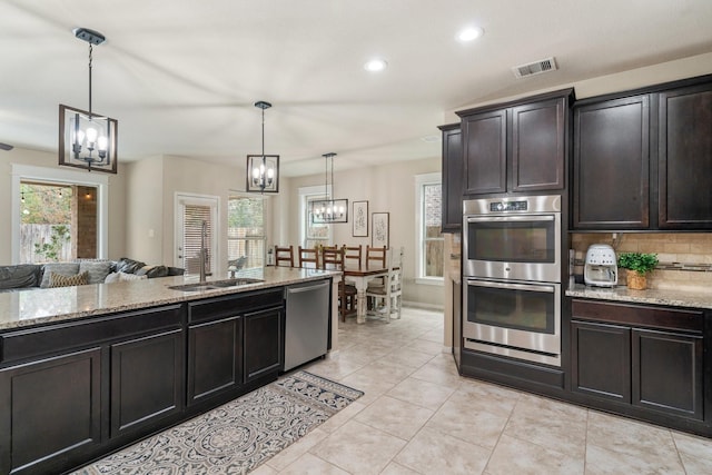 kitchen featuring stainless steel appliances, decorative light fixtures, a chandelier, and light stone countertops