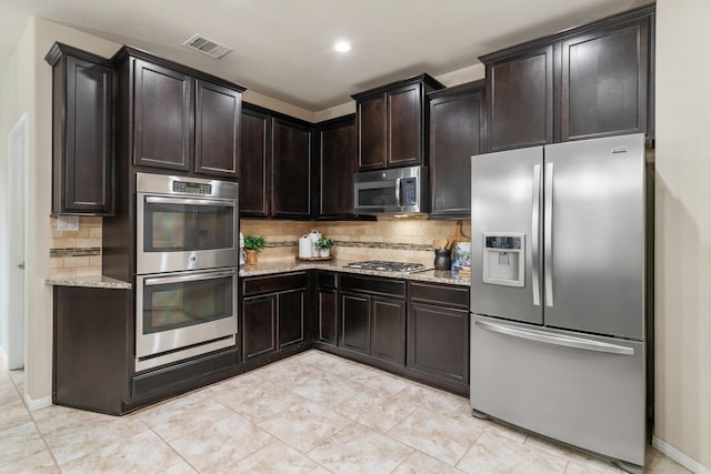 kitchen featuring decorative backsplash, light tile patterned floors, dark brown cabinetry, light stone counters, and stainless steel appliances