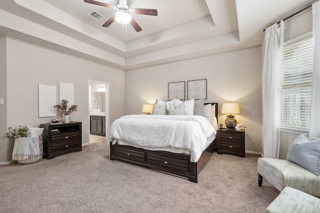 bedroom featuring ceiling fan, light colored carpet, ensuite bath, and a tray ceiling