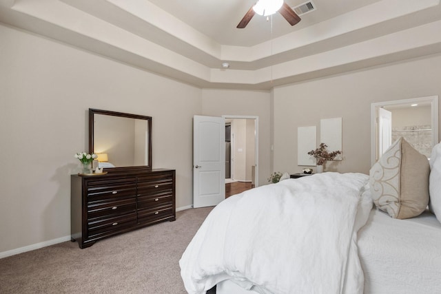 carpeted bedroom featuring a raised ceiling, ensuite bathroom, and ceiling fan