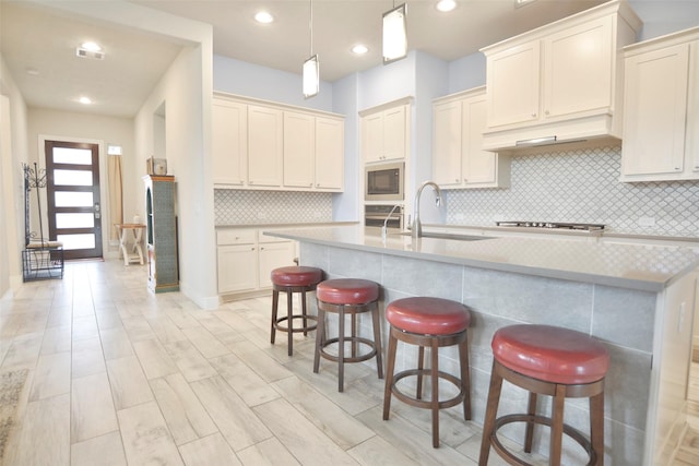 kitchen featuring a kitchen island with sink, a kitchen bar, built in microwave, and light countertops