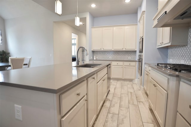 kitchen with pendant lighting, appliances with stainless steel finishes, wood tiled floor, a sink, and under cabinet range hood